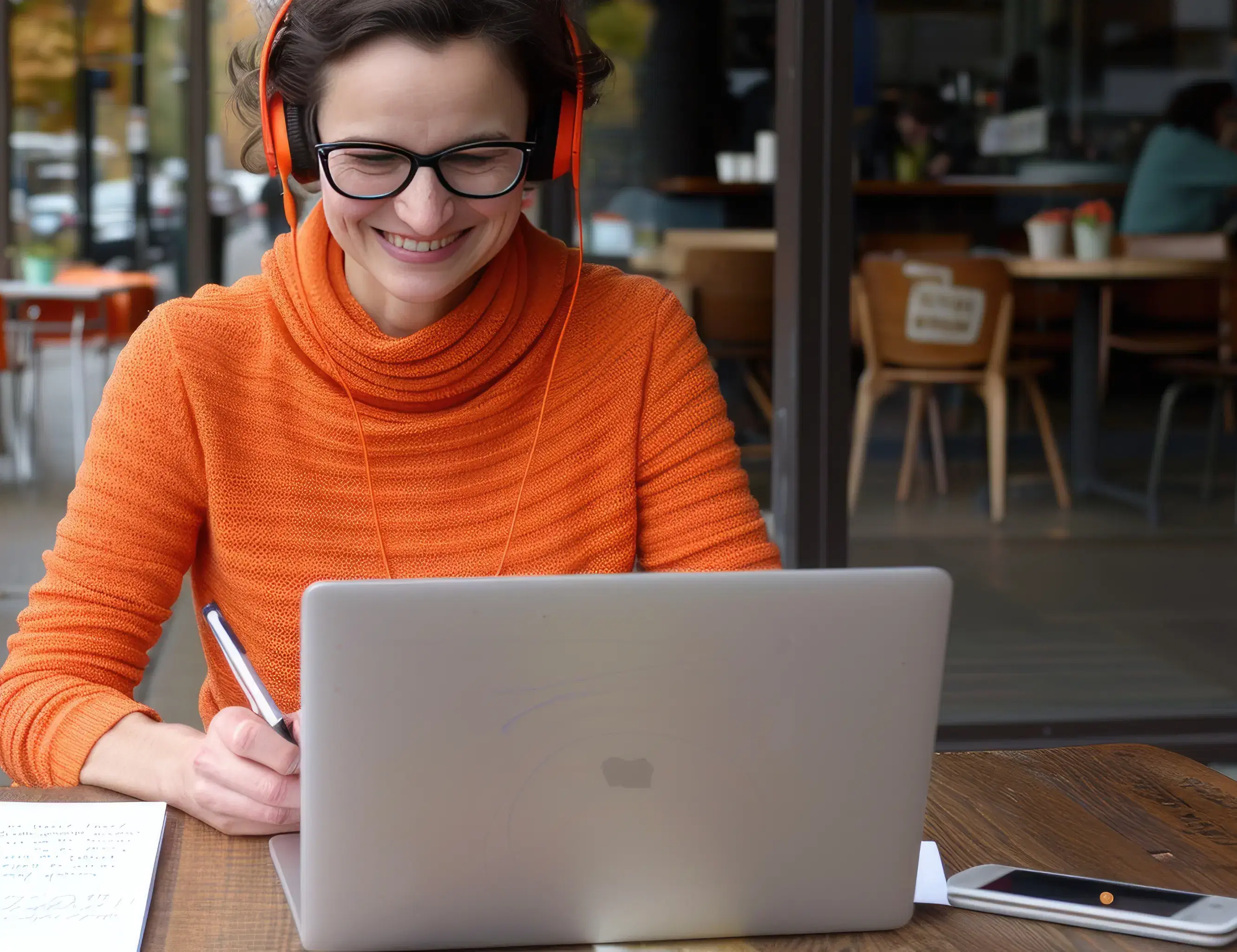 Smiling woman with headphones working on a laptop in a café